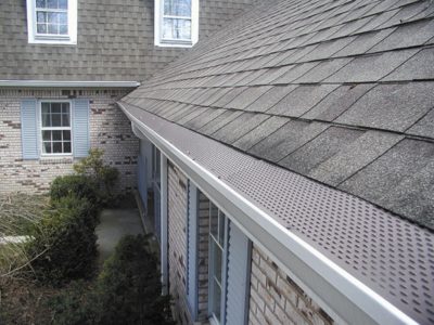 Gutters with gutter guards at the edge of a white brick home with pale blue shutters.