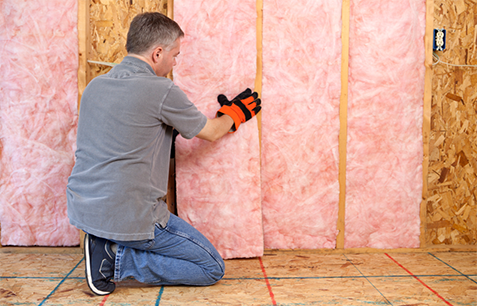 Technician installing pink fiberglass batt insulation in a wall.