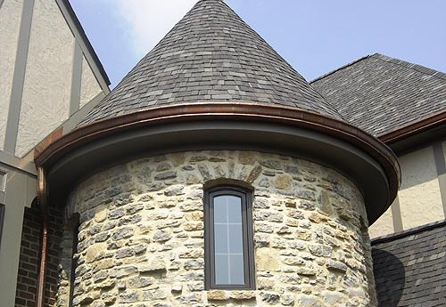 Gutter installation on a round turret of a stone-and-stucco home.