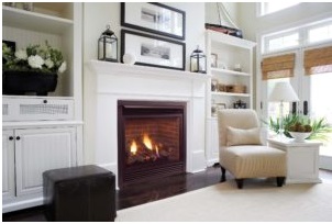Fireplace lit in living room with white surrounding mantel and built-in shelves, and white rug on dark wood floor.
